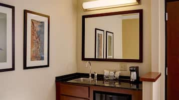 Casa de banho de hotel com lavatório, espelho, obra de arte emoldurada e máquina de café.
