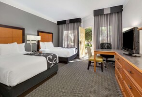 Habitación de hotel con dos camas, un escritorio, televisor y vistas al exterior.