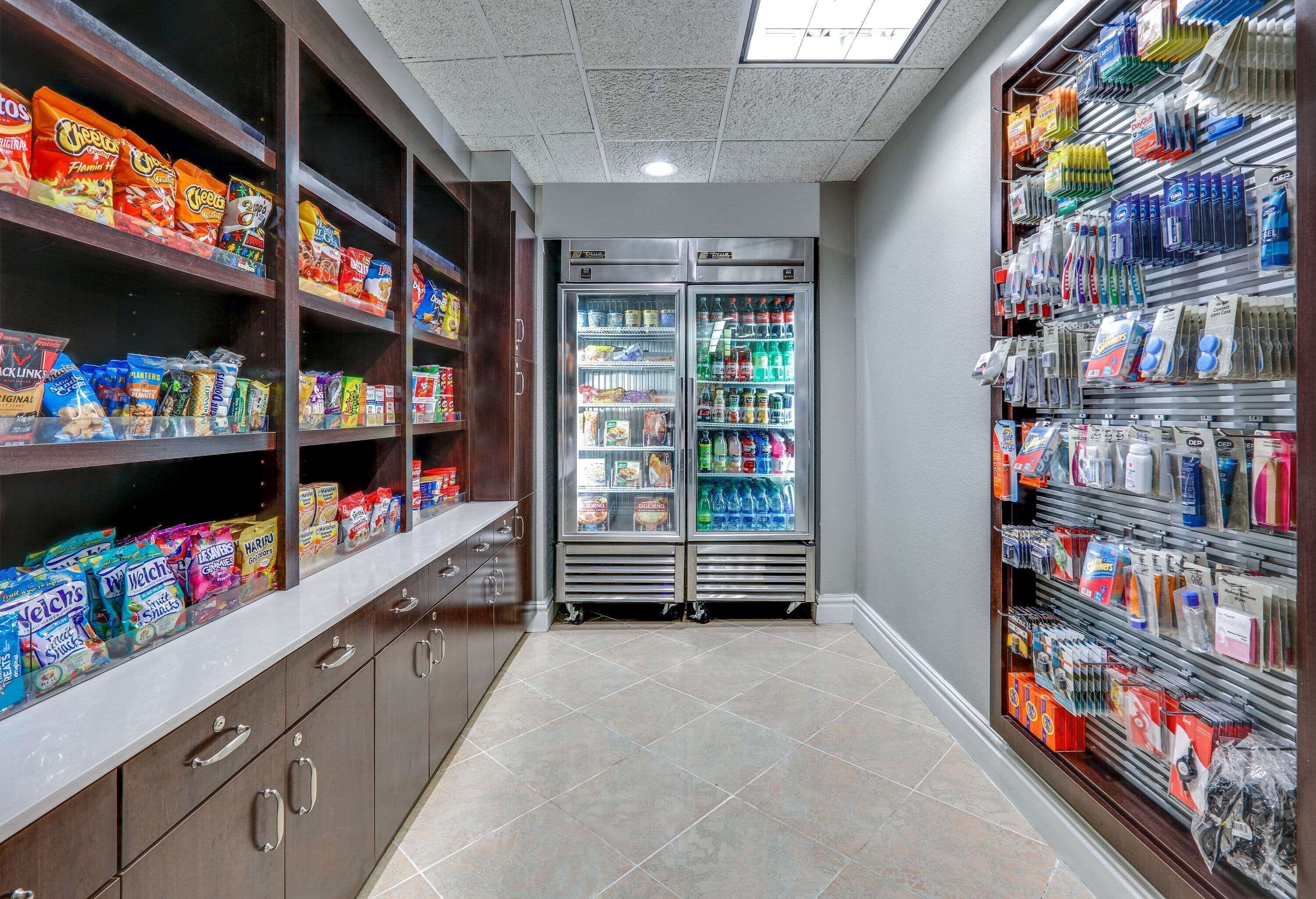 Una tienda de comestibles con estantes llenos de bocadillos y bebidas, una sección refrigerada y una exhibición de artículos de tocador.