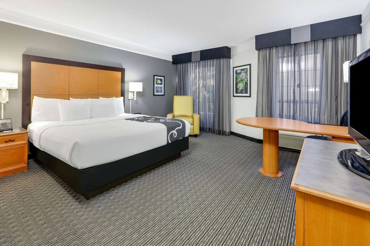 A hotel room with a large bed, a desk, a chair, and a television.