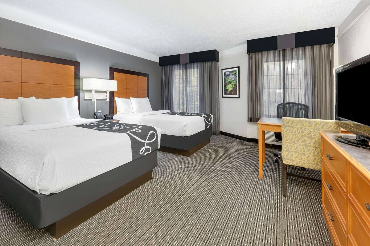 A hotel room with two beds, a desk, a television, and a chair.