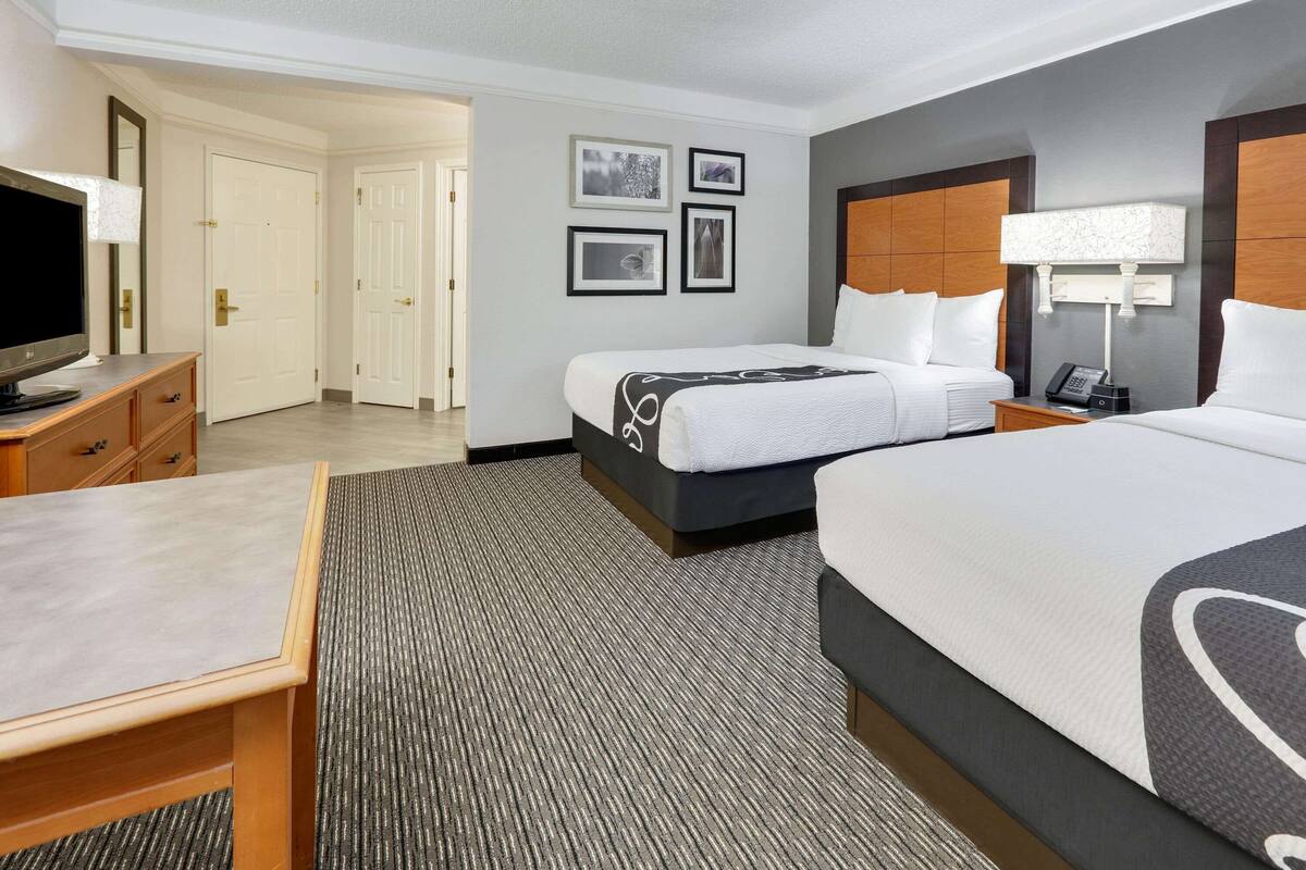 A hotel room with two beds, a desk, a TV, and a lamp.