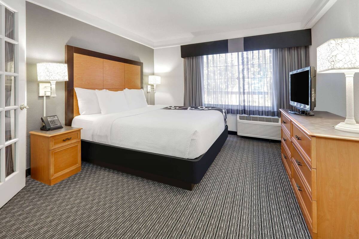 A hotel room with a large bed, bedside lamps, a TV, a desk with a lamp, and a dresser.