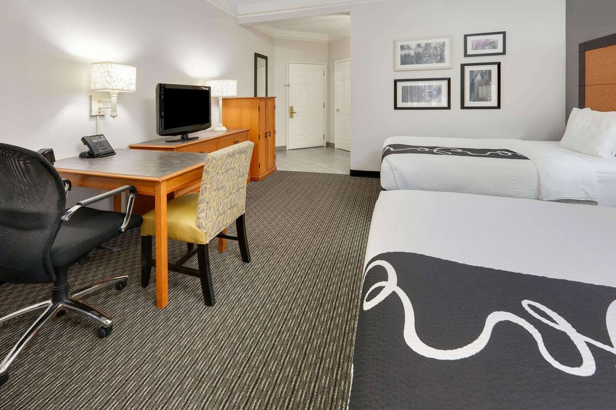 A hotel room with a bed, a desk with a computer, a chair, a lamp, and a television.