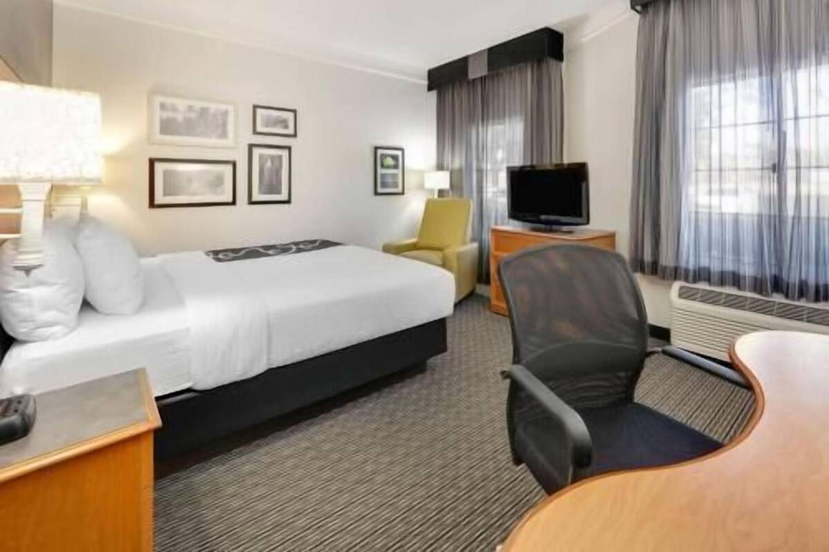 A hotel room with a bed, a desk, a chair, a television, and framed pictures on the wall.