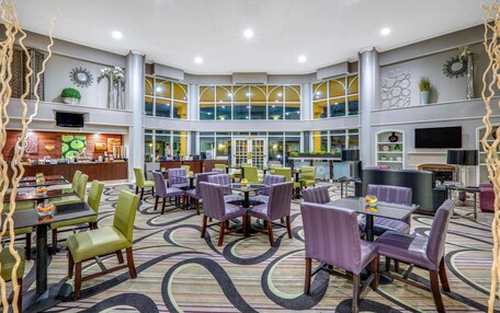 A spacious hotel lobby with multiple seating areas, a central bar, and a large windowed wall providing views.