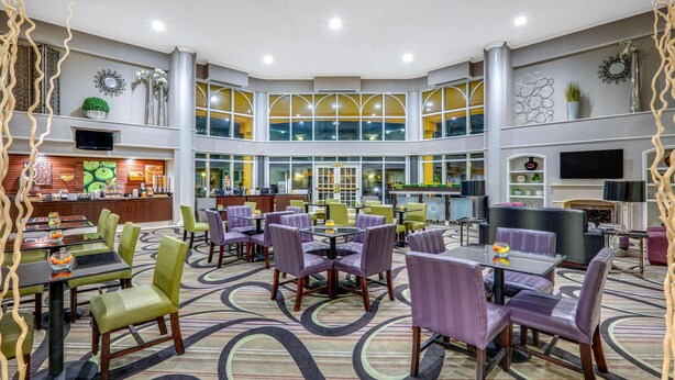 En rummelig hotellobby med flere siddeområder, en central bar og en stor vinduesvæg med udsigt.