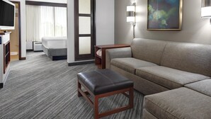 Habitación de hotel con sofá, una mesita de madera, una banca, televisor, cama, un cuadro y una lámpara de pared.