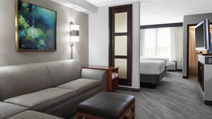 Habitación de hotel con sofá, una mesita de madera, cama, televisión y un cuadro en la pared.