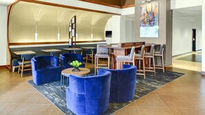 Un vestíbulo moderno con asientos azules, una zona de bar y un cuadro abstracto de gran tamaño.