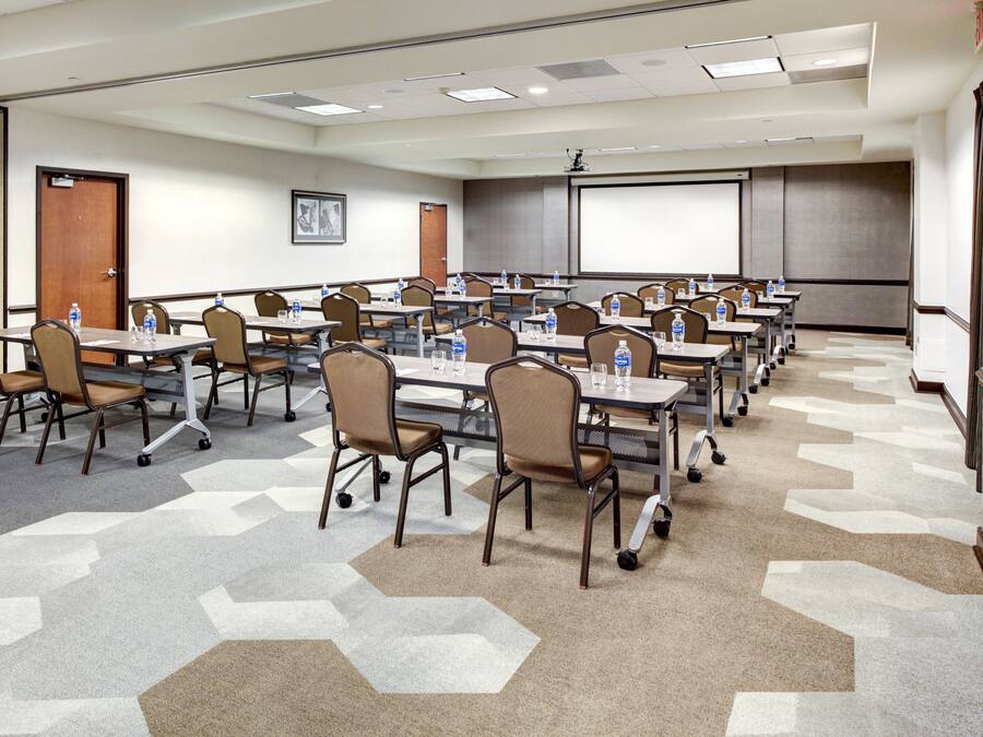 Un salón de conferencias con varias mesas y sillas, equipado con botellas de agua y vasos.