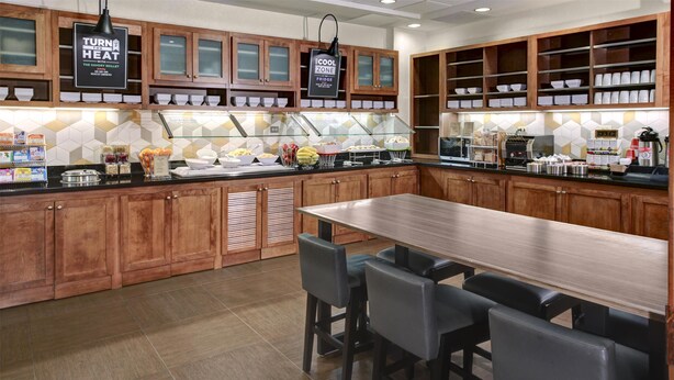 Una cocina moderna con armarios de madera, una isla central con taburetes de bar y una vitrina de vidrio con productos alimenticios.