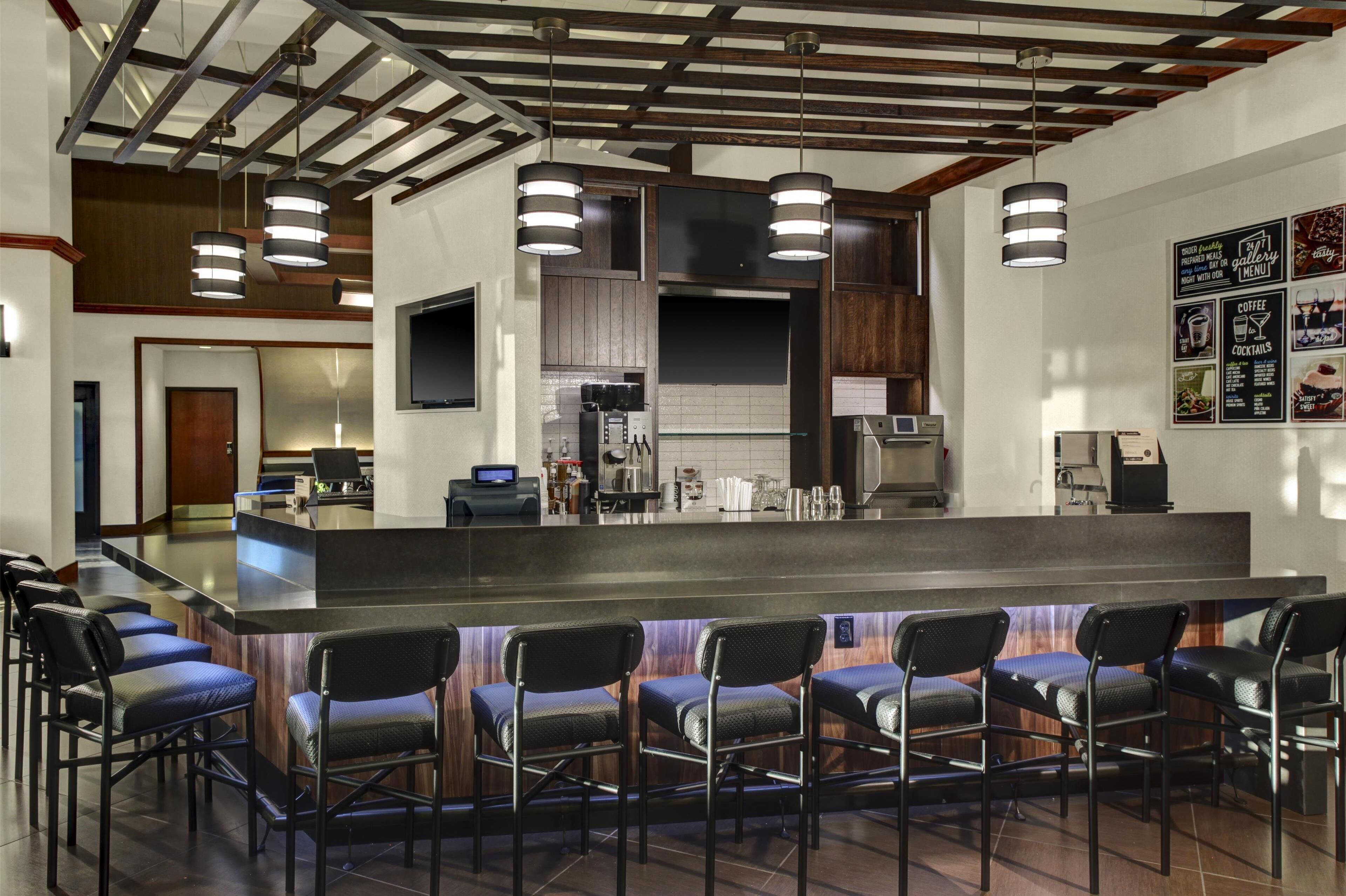 A modern bar area with a long counter, multiple bar stools, and overhead lighting.