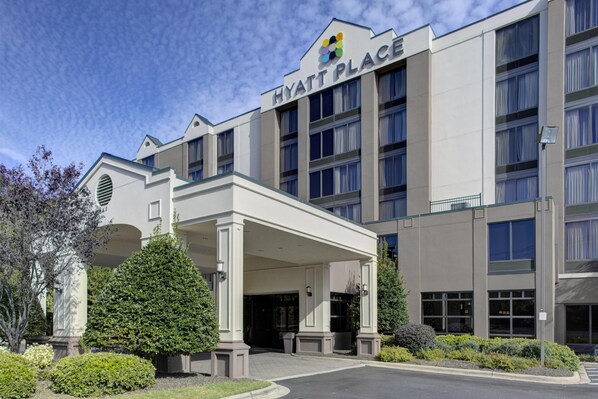 A modern hotel with a covered entrance, multiple floors, and a clear sky.