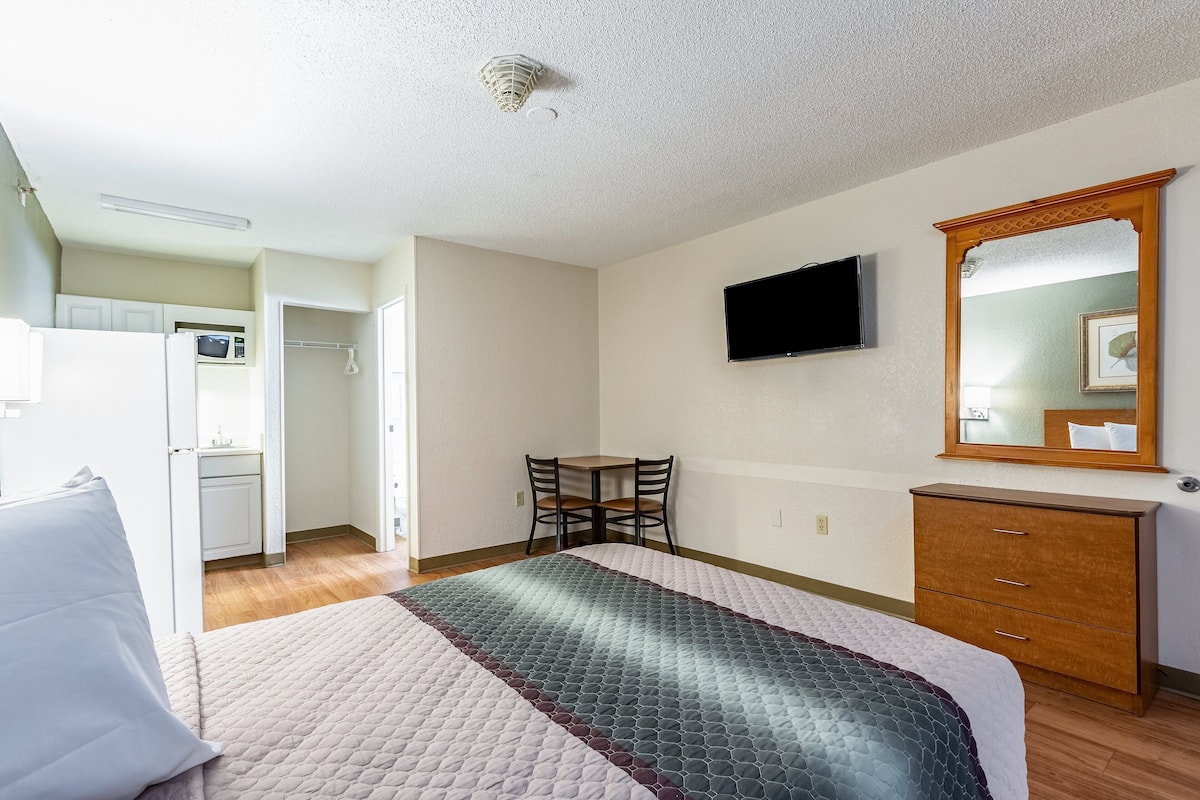 A bedroom with a bed, a dresser, a TV, and a small dining area.