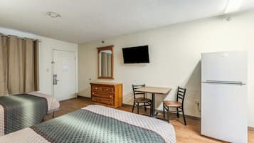 A hotel room with a bed, a desk, a chair, a dresser, a television, and a refrigerator.