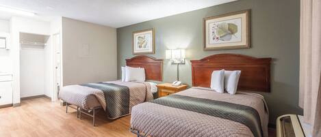 A hotel room with two beds, a wooden floor, a ceiling light, and a wall-mounted air conditioning unit.