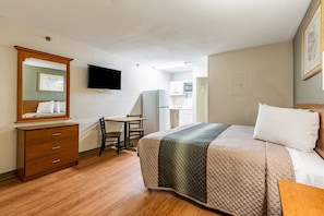 Habitación de hotel con cama, escritorio, silla, cómoda, televisor de pantalla plana y kitchenette.
