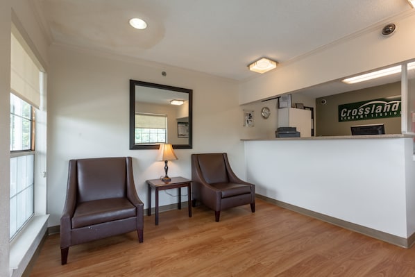 A reception area with two leather chairs, a small table with a lamp, and a reception desk with a sign that reads "Crossland Economy Studios." - HomeTowne Studios by Red Roof Atlanta - Norcross South (Norcross)