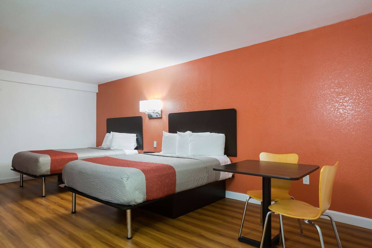A hotel room with two beds, a table, and a chair.