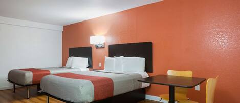 A hotel room with two beds, a table, and a chair.