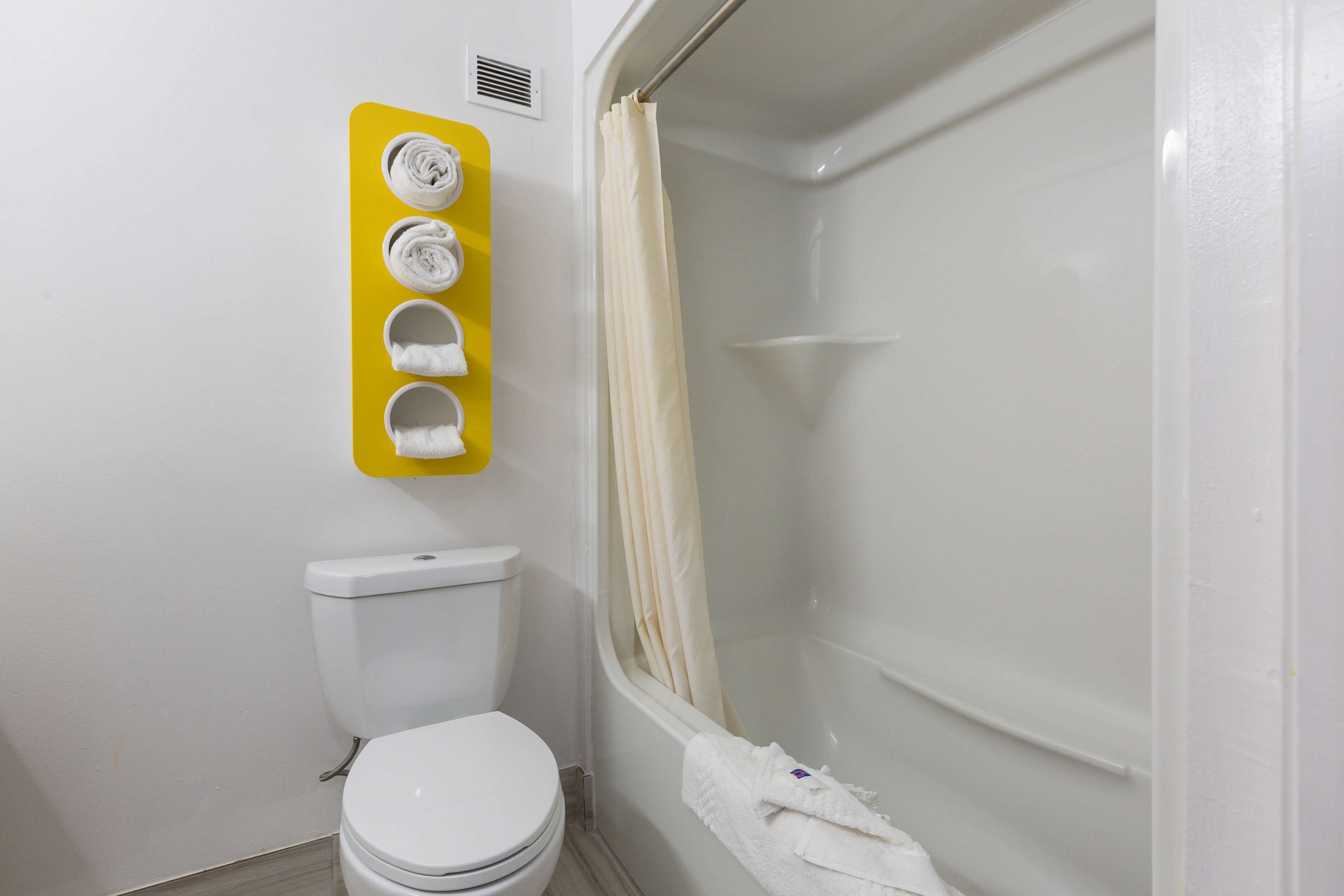 Une salle de bain équipée de toilettes, d’une douche et d’un porte-serviettes jaune sur lequel sont disposées quatre serviettes.
