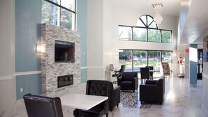 A spacious indoor area with a stone fireplace, comfortable seating, and large windows offering views of the outdoors. - Motel 6 Suwanee, GA - Gwinnett Center (Suwanee)