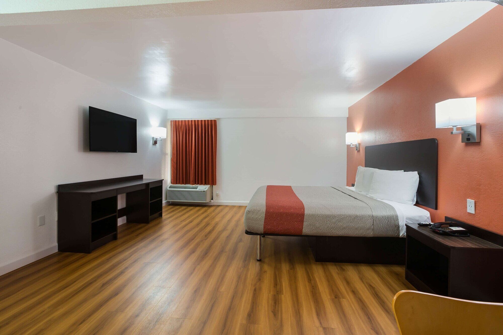 A hotel room with a bed, bedside table, TV, and a desk with a chair.