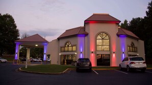 A building with a covered entrance, large windows, and a parking lot with cars. - Motel 6 Suwanee, GA - Gwinnett Center (Suwanee)