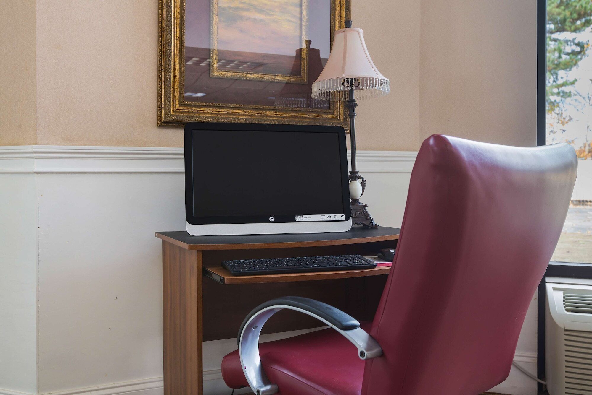 A computer desk with a monitor, keyboard, and a red office chair.