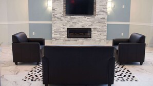 A modern living room with a stone fireplace, two leather sofas, a flat-screen TV, and a patterned rug. - Motel 6 Suwanee, GA - Gwinnett Center (Suwanee)
