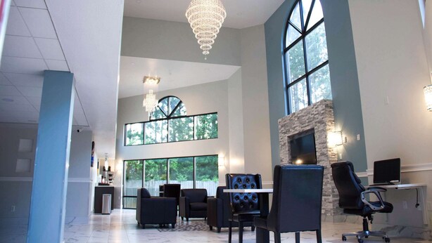 A spacious interior with a high ceiling, a chandelier, a fireplace, and large windows. - Motel 6 Suwanee, GA - Gwinnett Center (Suwanee)