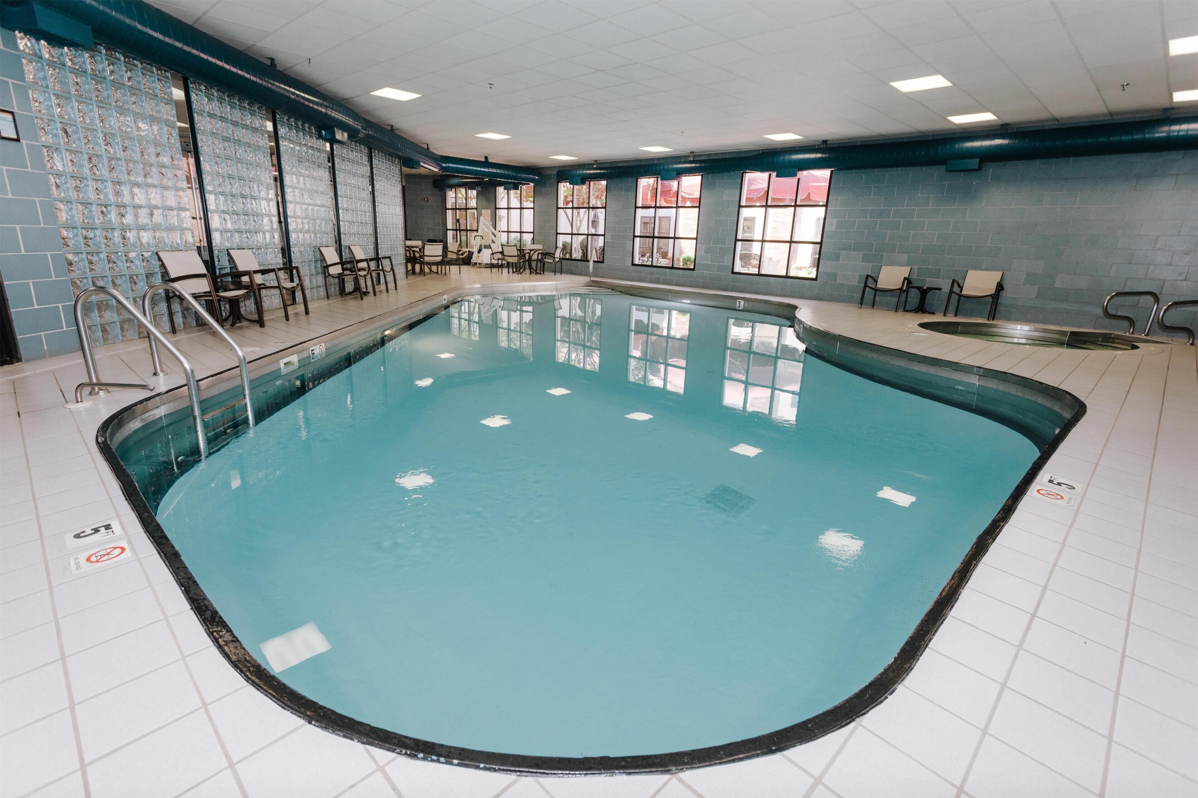 An indoor swimming pool with tiled walls, windows, and lounge chairs.