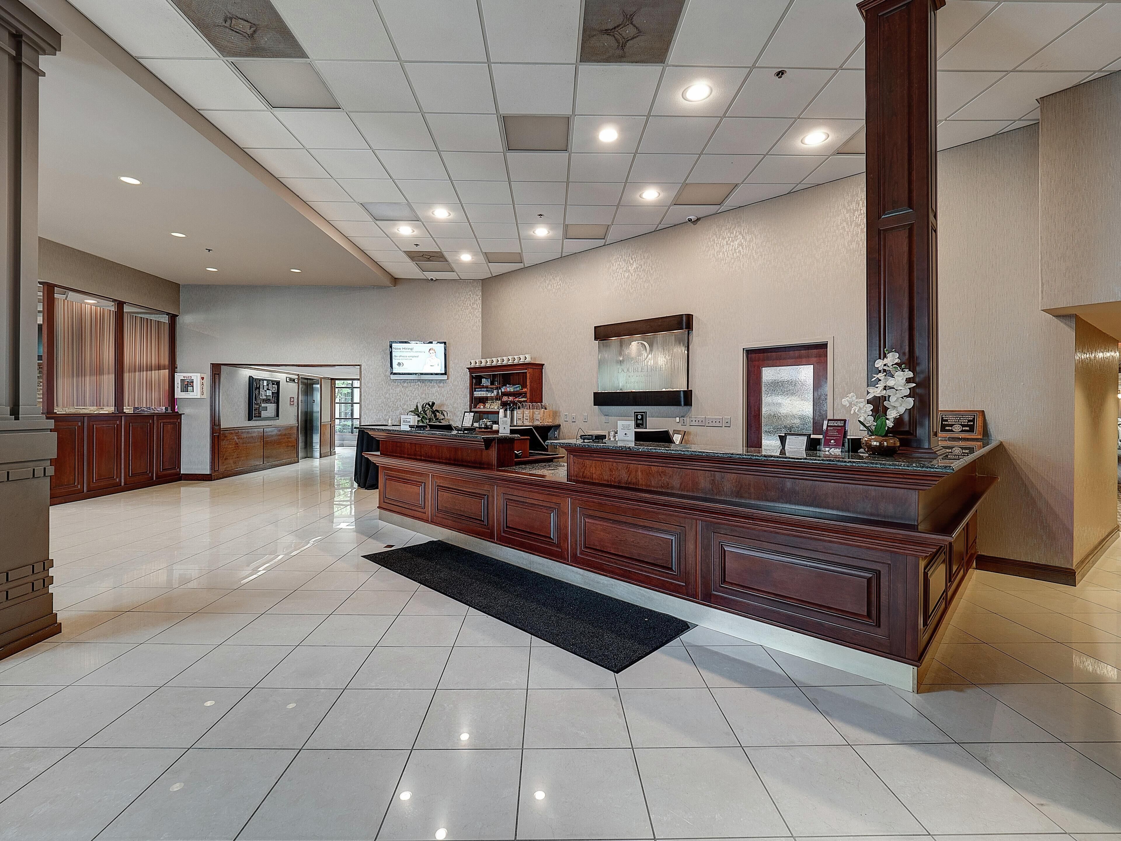 A hotel lobby with a reception desk, a digital screen, and a large mirror.