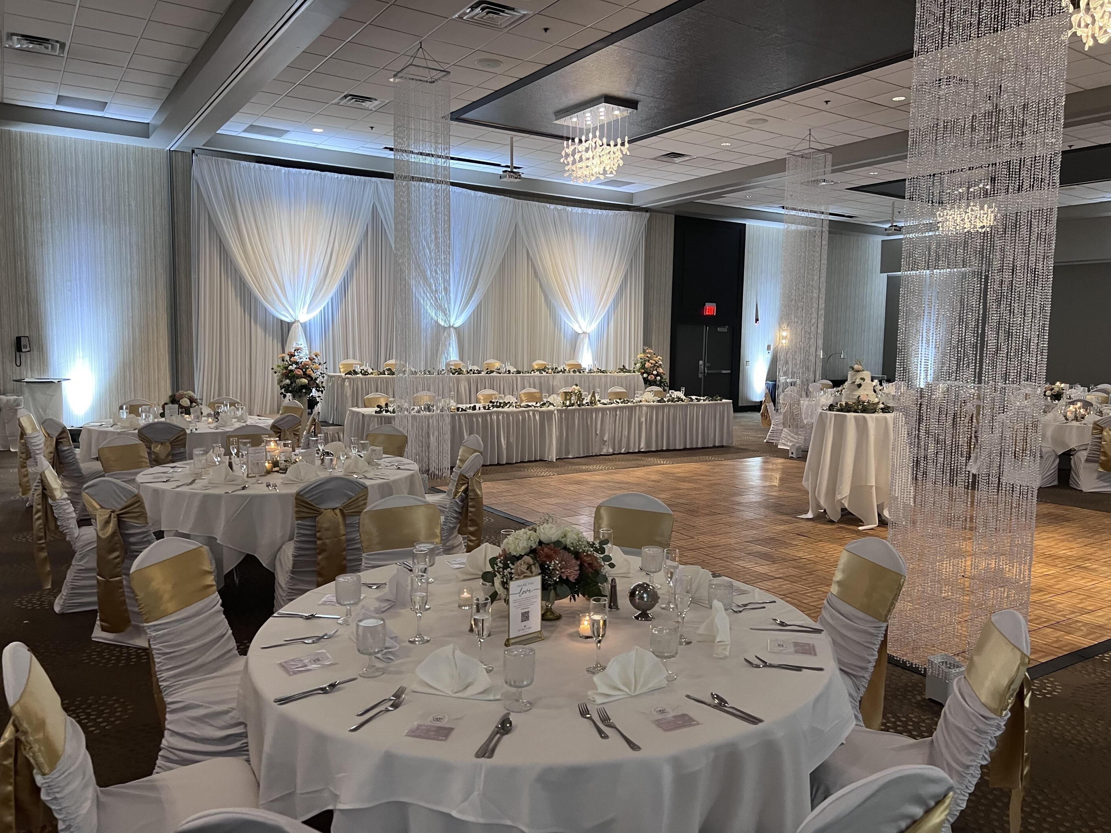 A banquet hall with round tables, white tablecloths, and gold sashes.