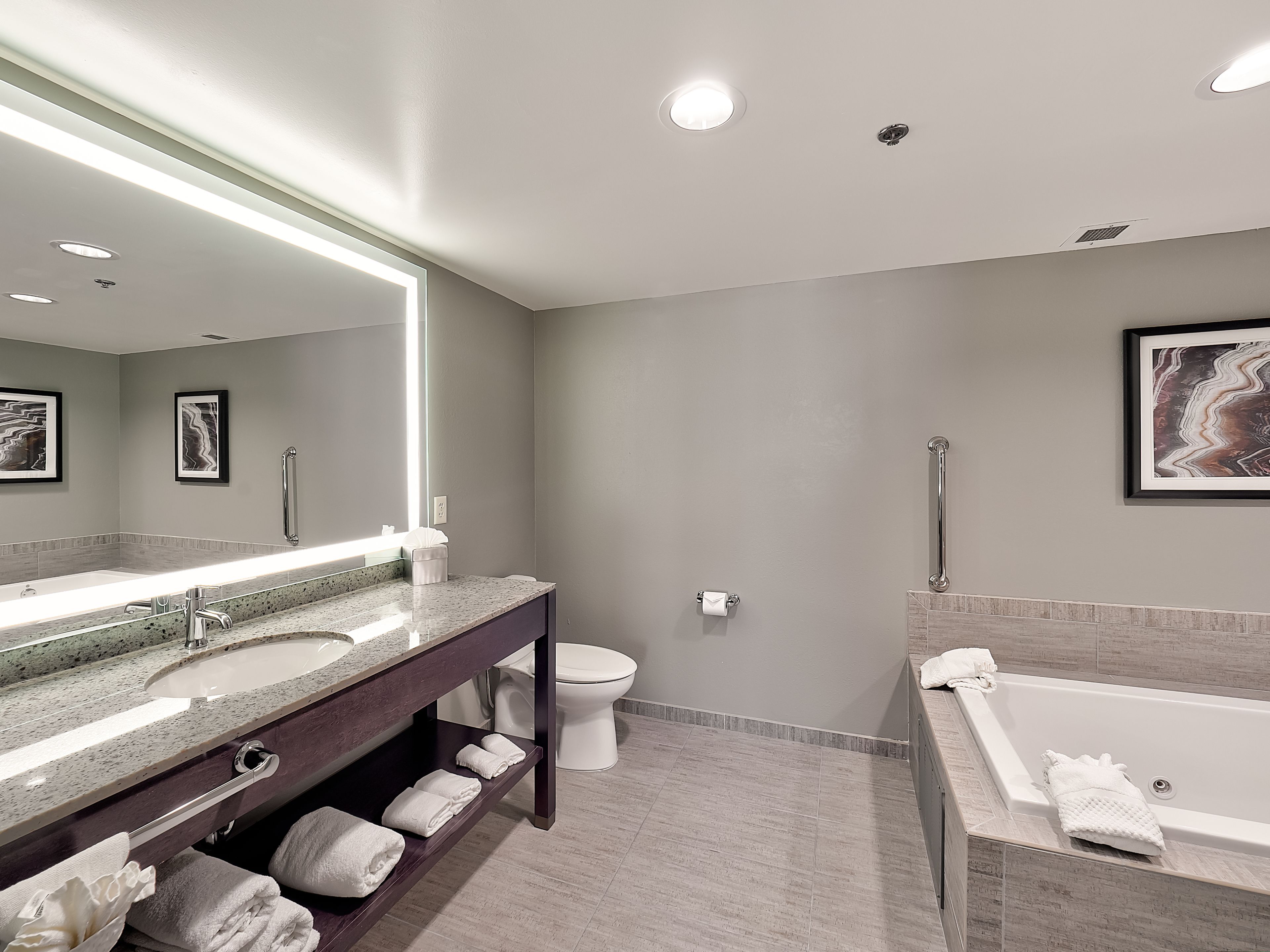 Une salle de bain moderne avec un grand miroir, une baignoire, des toilettes et un meuble-lavabo.