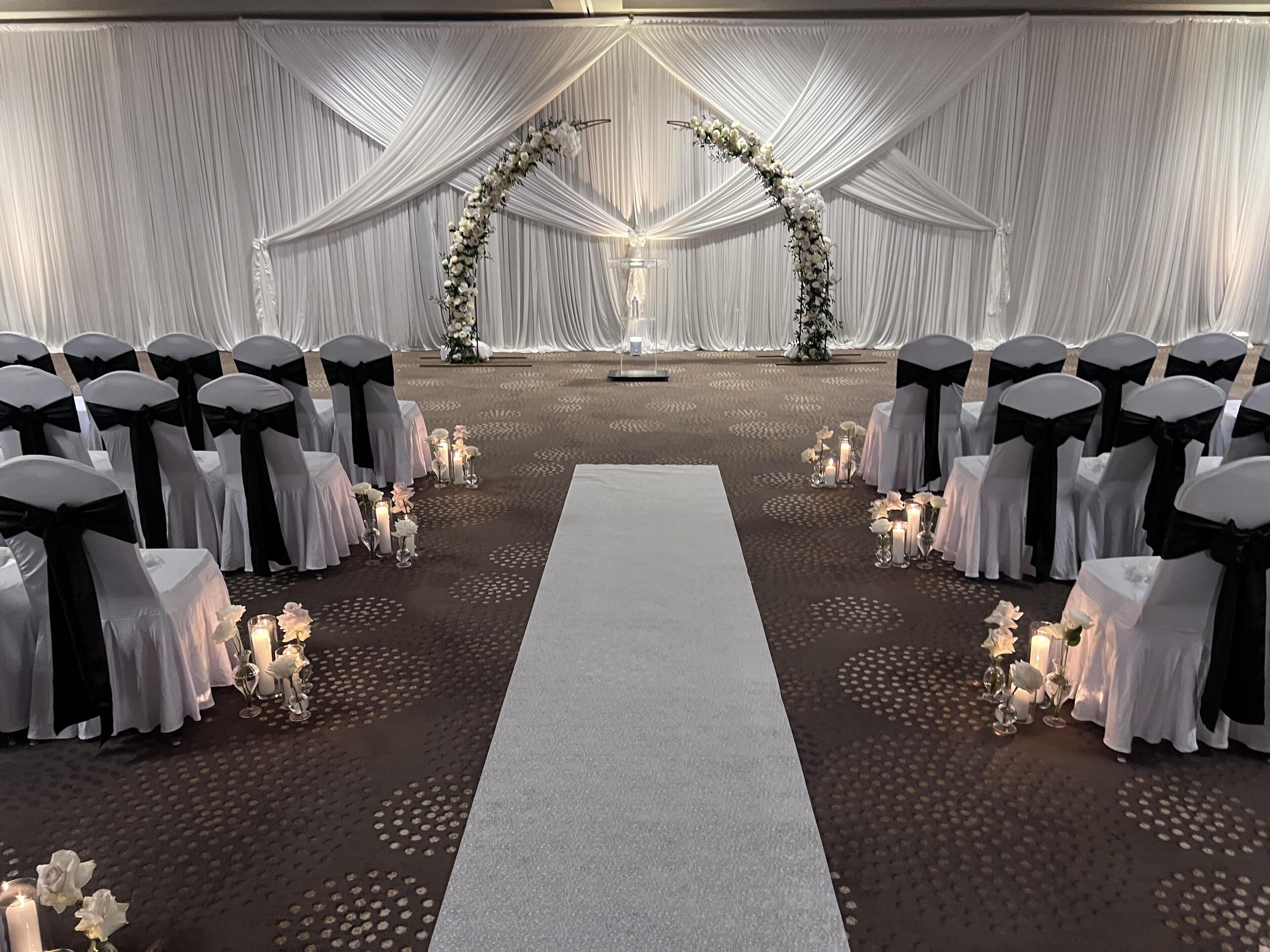 Un salón de bodas con hileras de sillas, un pasillo central y decoración floral.