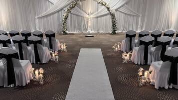 Un salón de bodas con hileras de sillas, un pasillo central y decoración floral.