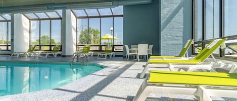 A swimming pool area with lounge chairs and tables, large windows, and a ceiling fan.