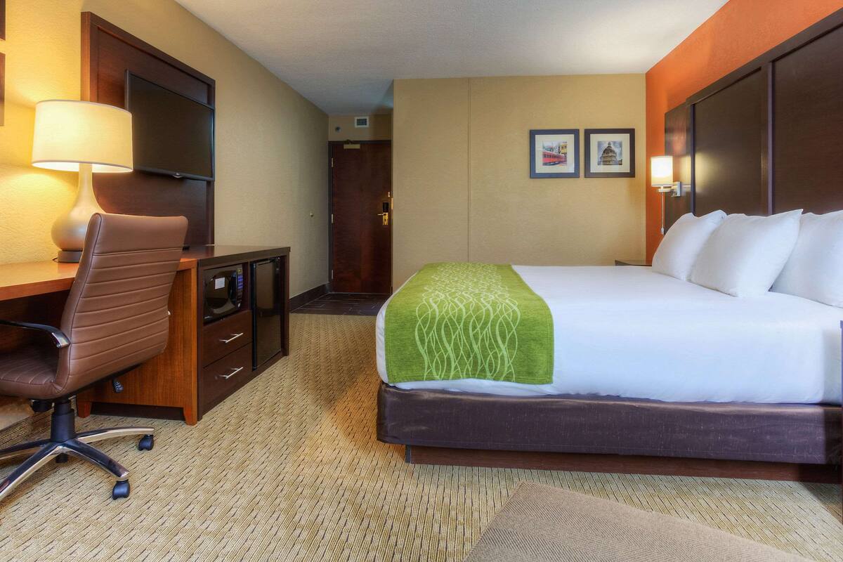 A hotel room with a bed, desk, chair, and a television.