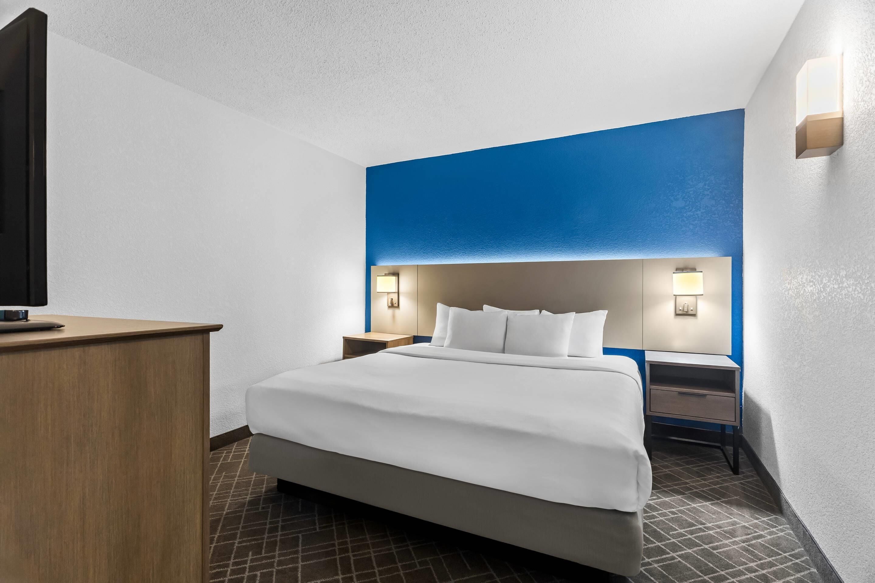 A hotel room with a bed, bedside tables, a desk, and a television.