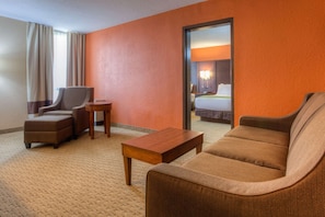 A hotel room with a brown sofa, a chair, a small wooden table, and a bed with a white headboard. - Comfort Inn & Suites Evansville Airport (Evansville)