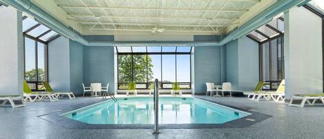 An indoor swimming pool with clear glass ceilings, white walls, and a view of trees outside.