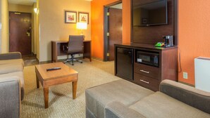 Habitación de hotel con sofá, una mesita, escritorio con silla, televisor y microondas.
