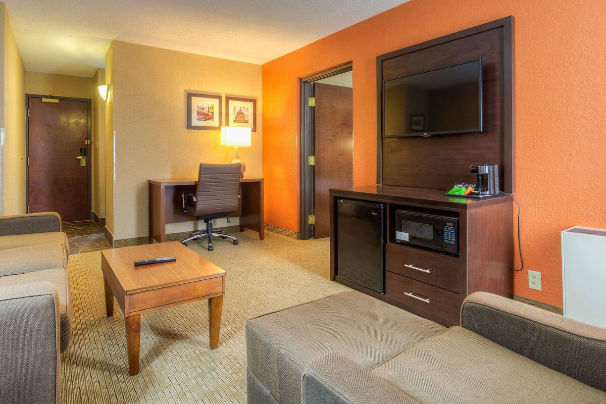 A hotel room with a sofa, a small table, a desk with a chair, a television, and a microwave.