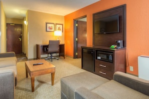 Ein Hotelzimmer mit Sofa, kleinem Tisch, Schreibtisch mit Stuhl, Fernseher und Mikrowelle.