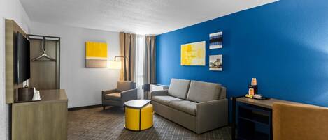 Habitación de hotel con sofá, sillón y una mesita de noche con lámpara.