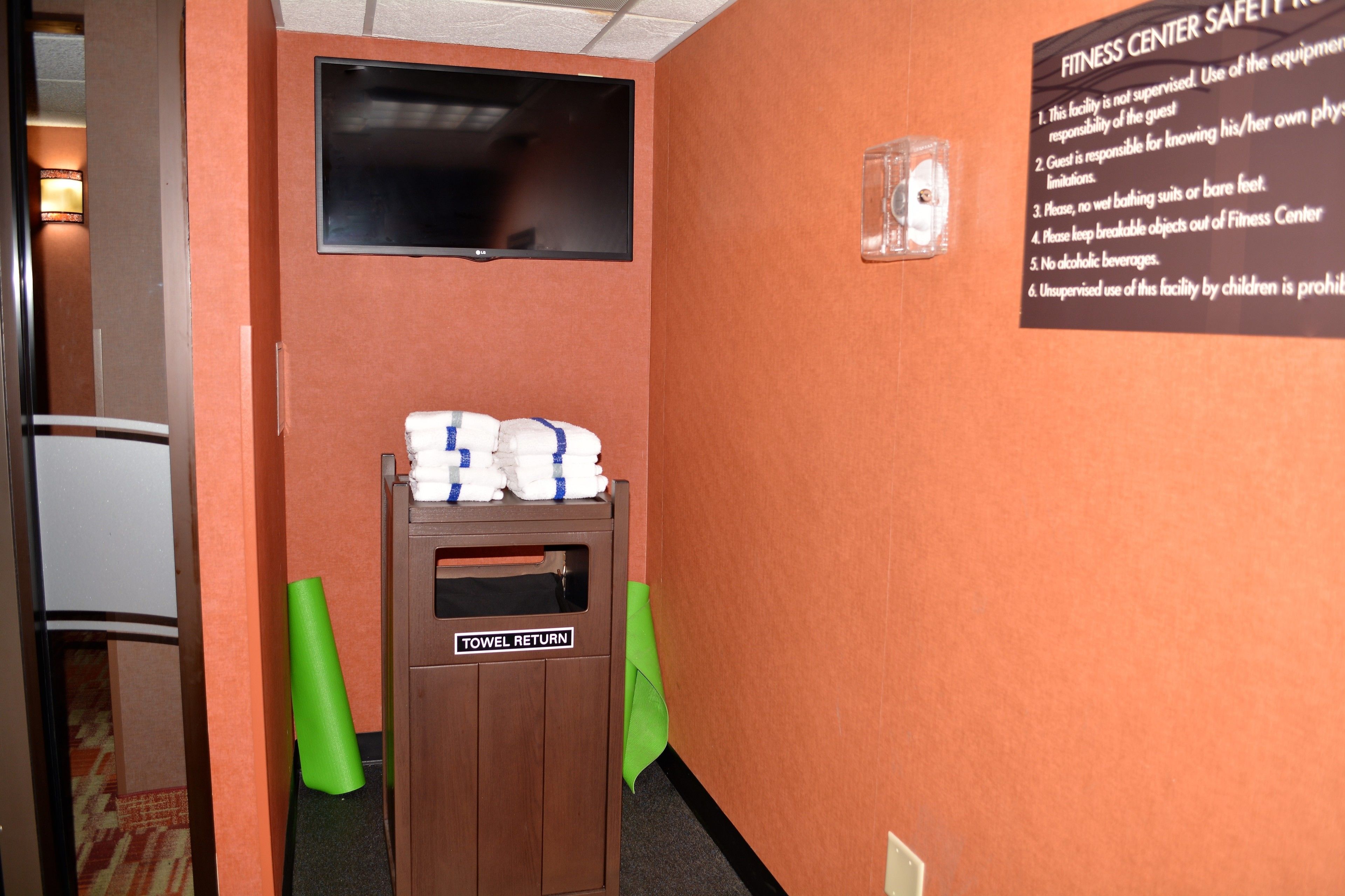 A fitness center with a towel return station, a wall-mounted television, and a safety sign.