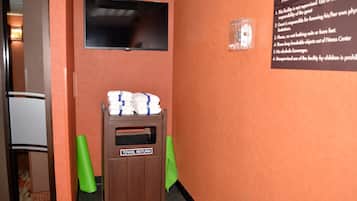 A fitness center with a towel return station, a wall-mounted television, and a safety sign.