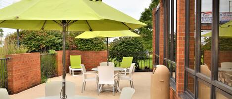 An outdoor patio area with round tables and white chairs, green umbrellas, and a brick wall.